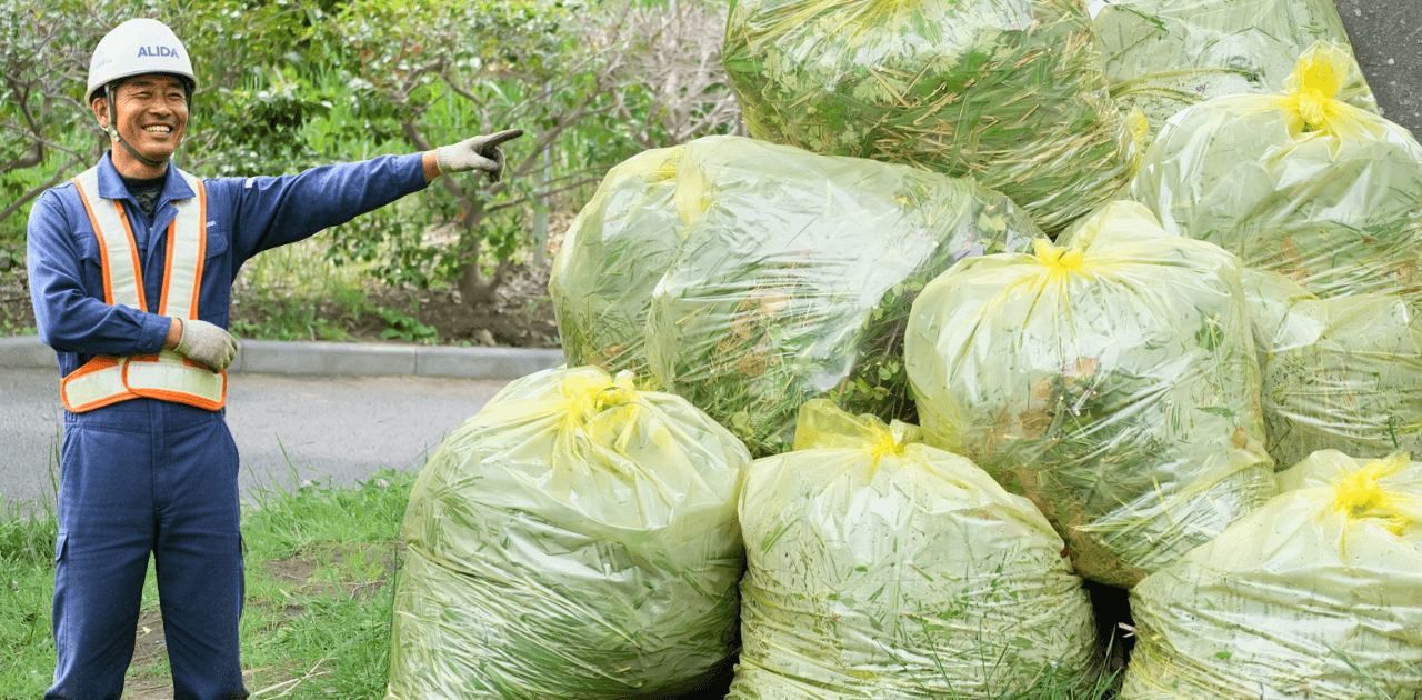 ゴミの山を指さす草刈りの職人